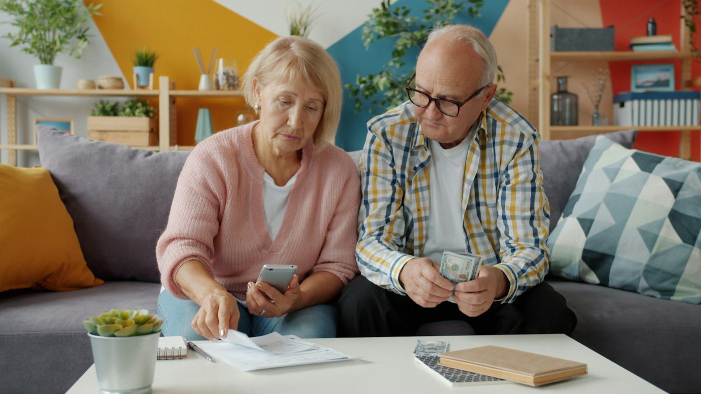 Senior couple comparing prescription costs with paperwork and a phone